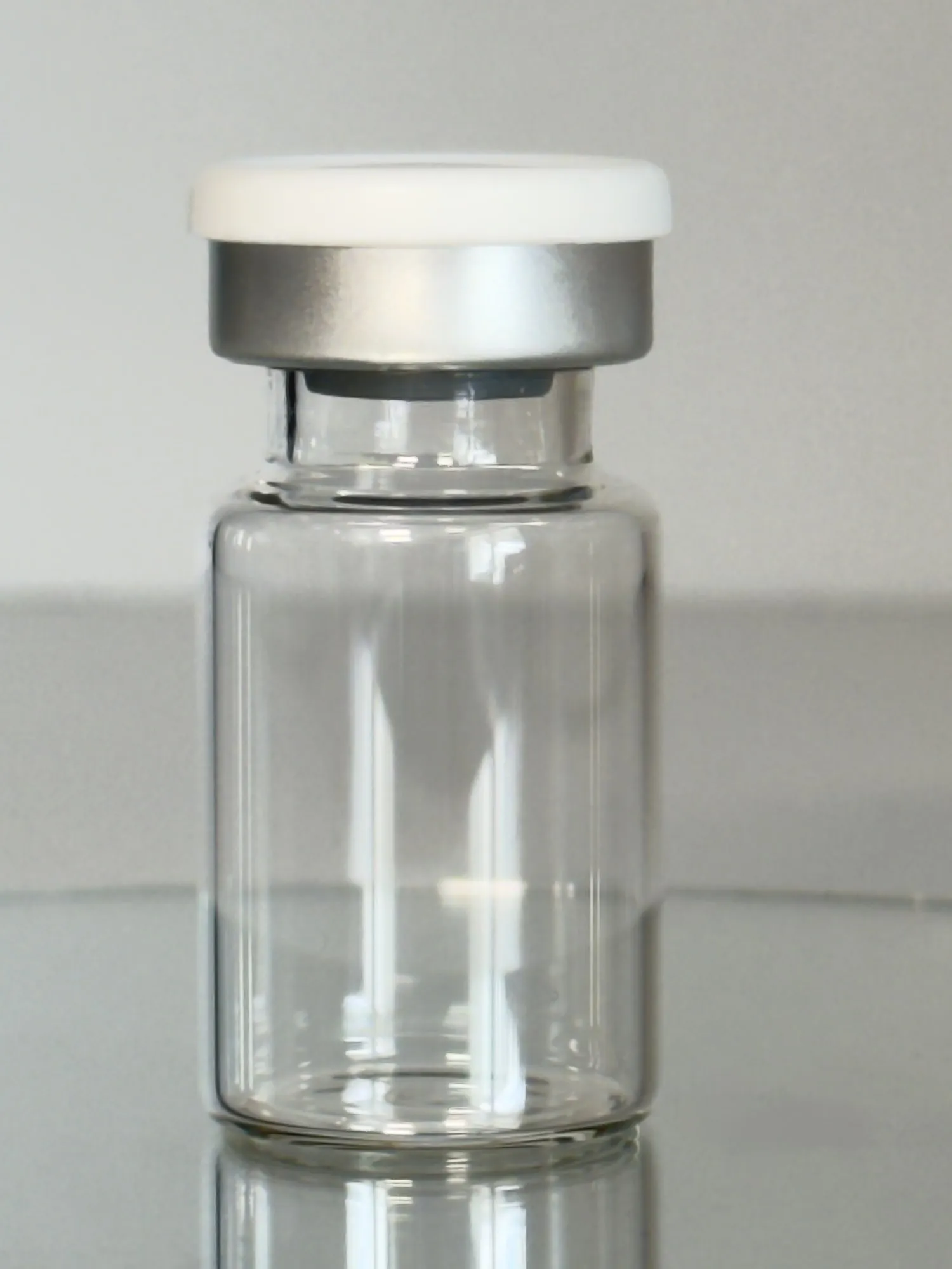 An empty DuraRad 6R serum vial with an aluminum crimp seal and white flip-off cap on a neutral gray surface.