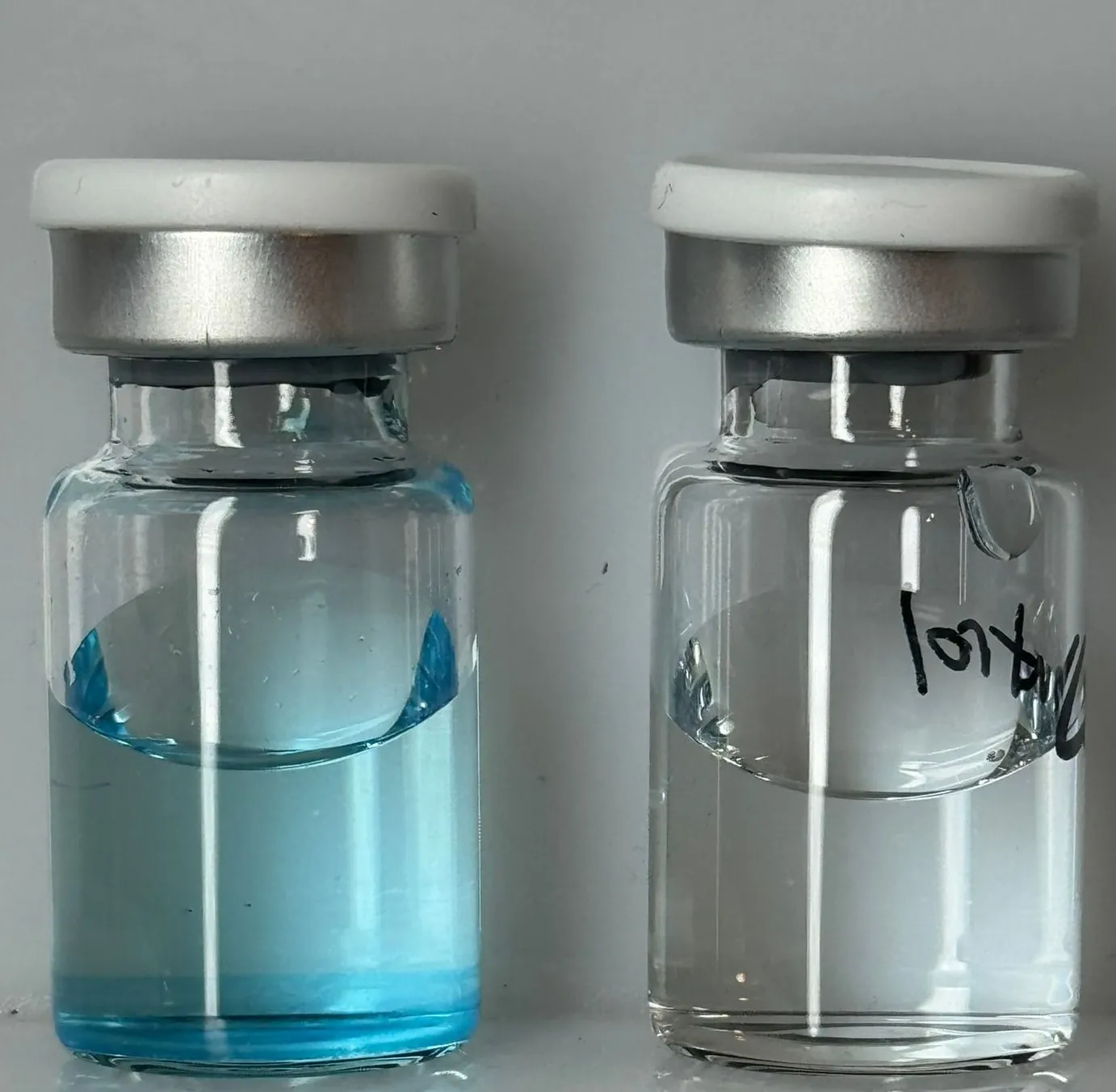 A bench functional test: a vial of blue methylene-blue dye at left beside a hand-labeled clear control vial at right — a qualitative demonstration of the coating's oxidative activity, not the DuraRad product or its color.
