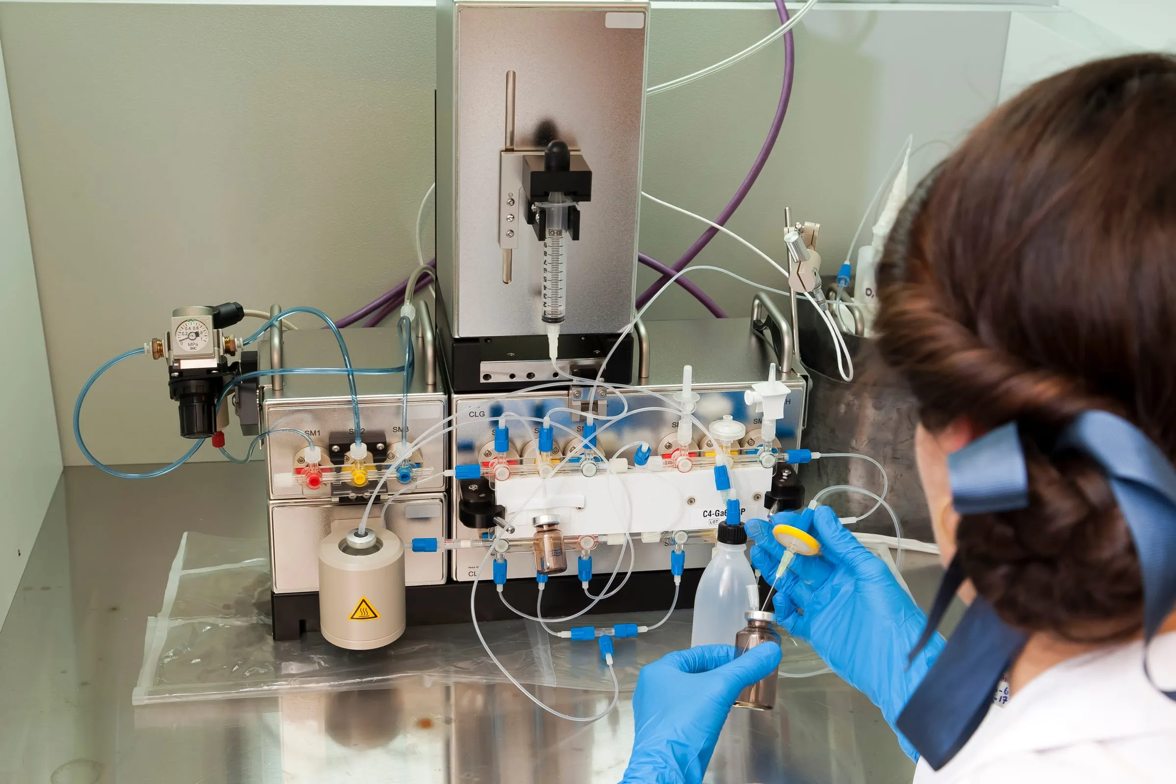 A gloved technician working at an automated radiopharmaceutical synthesis module in a laboratory — illustrative generic radiopharmacy, not a FabUTech or partner facility.